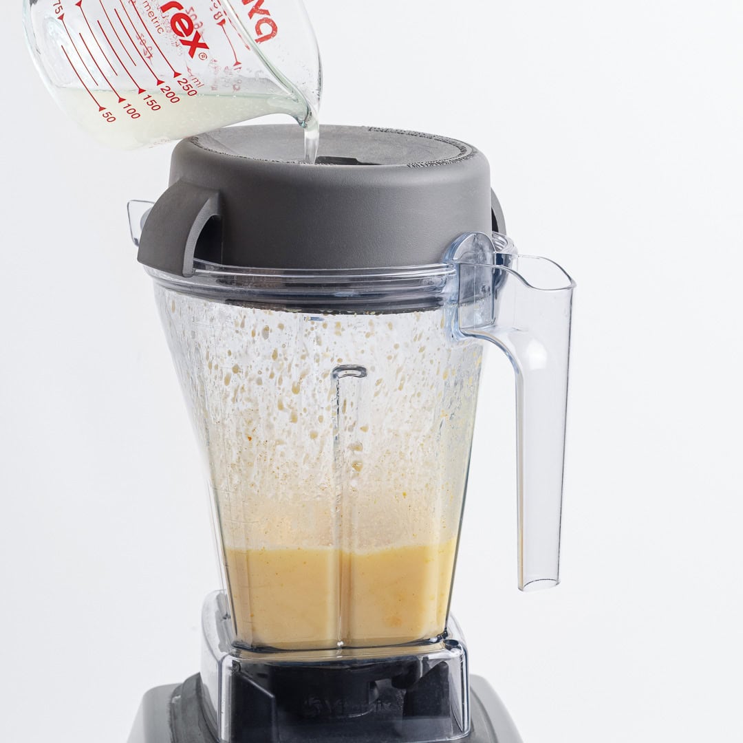 This homemade vegan butter melts, spreads and tastes like the real thing! Easy to make with everyday ingredients, you can even bake with it. Pouring lemon juice into blender with vegan butter.