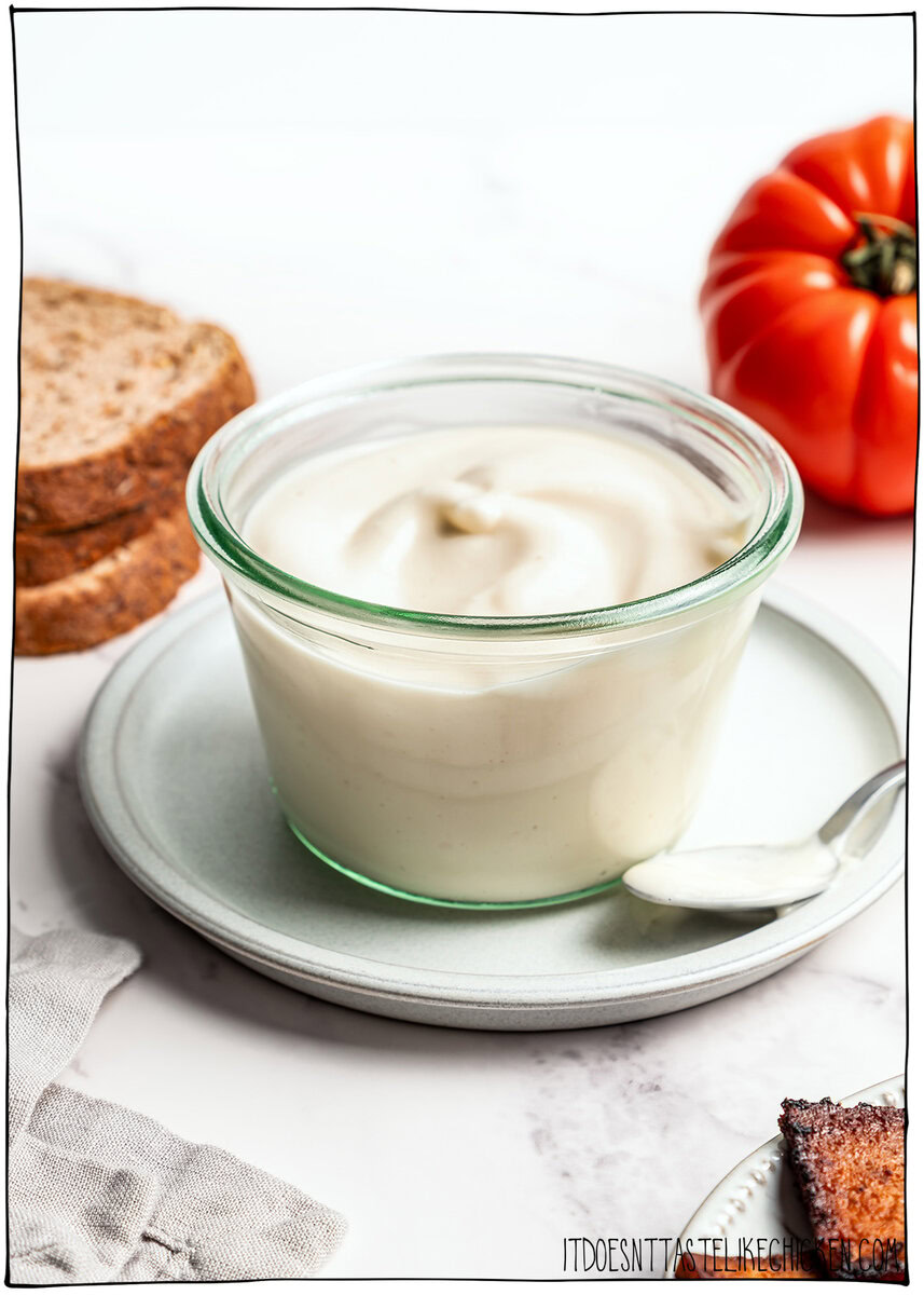 This thick, creamy vegan mayo is made in 5 minutes with soy milk! It’s the BEST fool-proof recipe, egg-free, and better than store-bought. Jar of vegan mayo on plate with spoon.