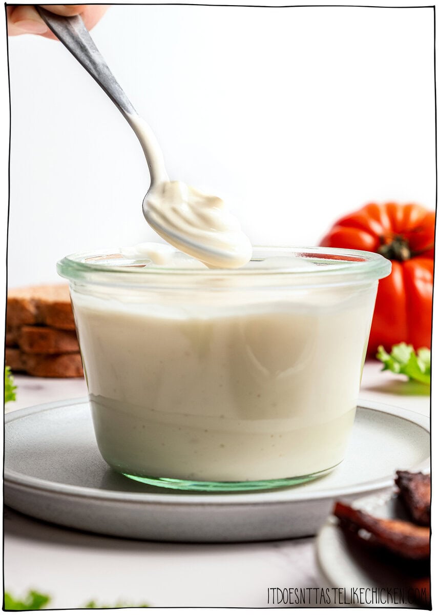 This thick, creamy vegan mayo is made in 5 minutes with soy milk! It’s the BEST fool-proof recipe, egg-free, and better than store-bought. Spoonful of vegan mayo held over jar.