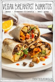Three stacked vegan breakfast burritos on plate showing tofu potatoes and vegetables inside.