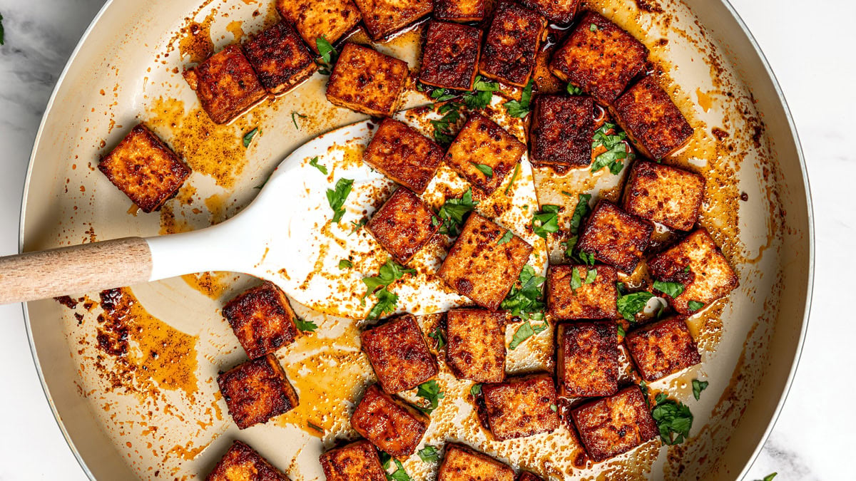 Browned tofu being cooked in a pan with cilantro garnish.