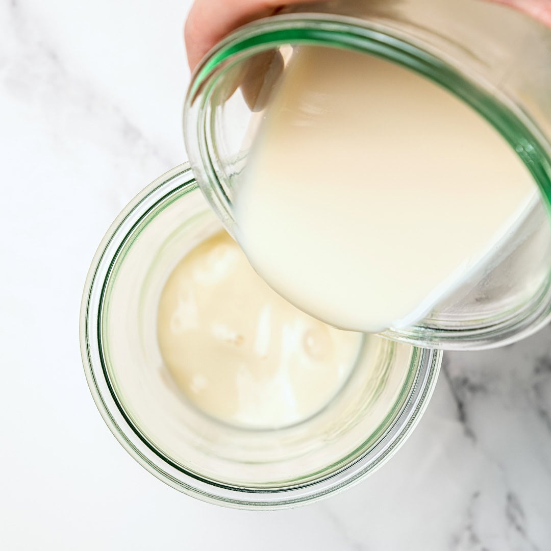 This thick, creamy vegan mayo is made in 5 minutes with soy milk! It's the BEST fool-proof recipe, egg-free, and better than store-bought. Pouring soy milk into jar for vegan mayo.