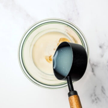 Pouring lemon juice into jar for vegan mayo.