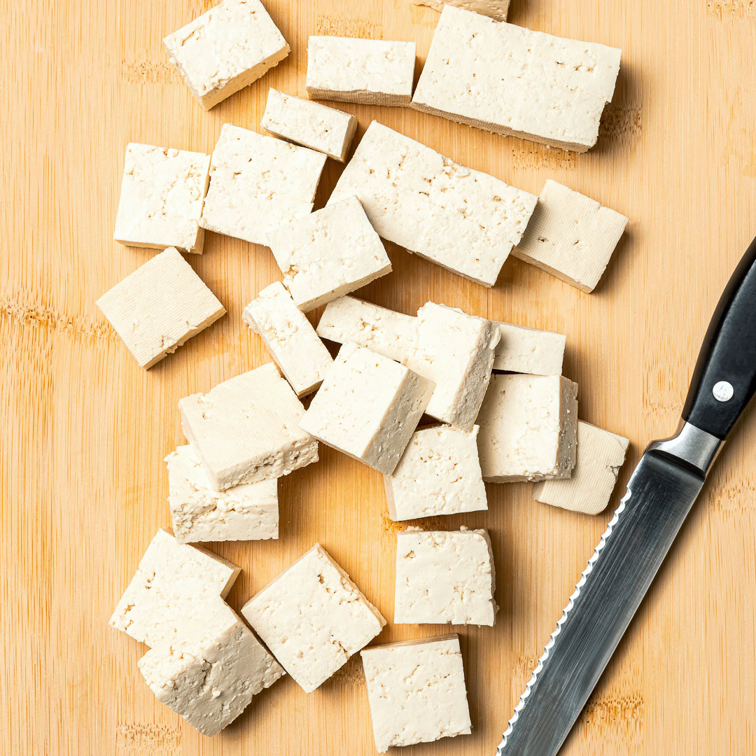 Tofu cubes on cutting board with knife.