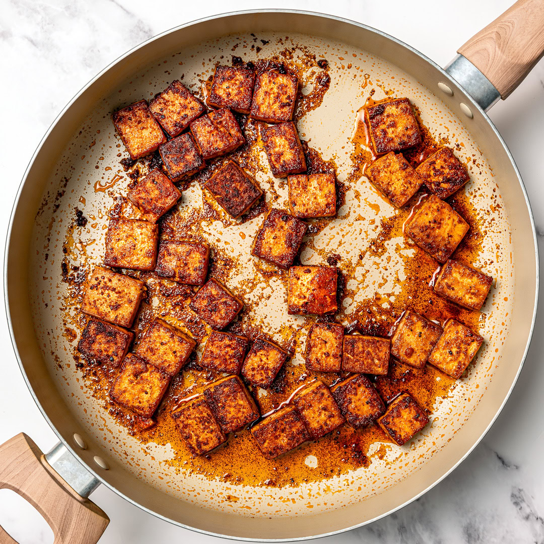 Marinated tofu cubes cooking in skillet.