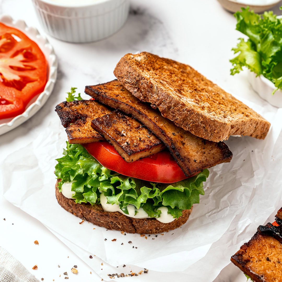 This vegan BLT is made with smoky plant-based bacon, juicy tomatoes, crisp lettuce, and creamy mayo. Easy, satisfying, and ready fast! Assembled vegan BLT on parchment paper.
