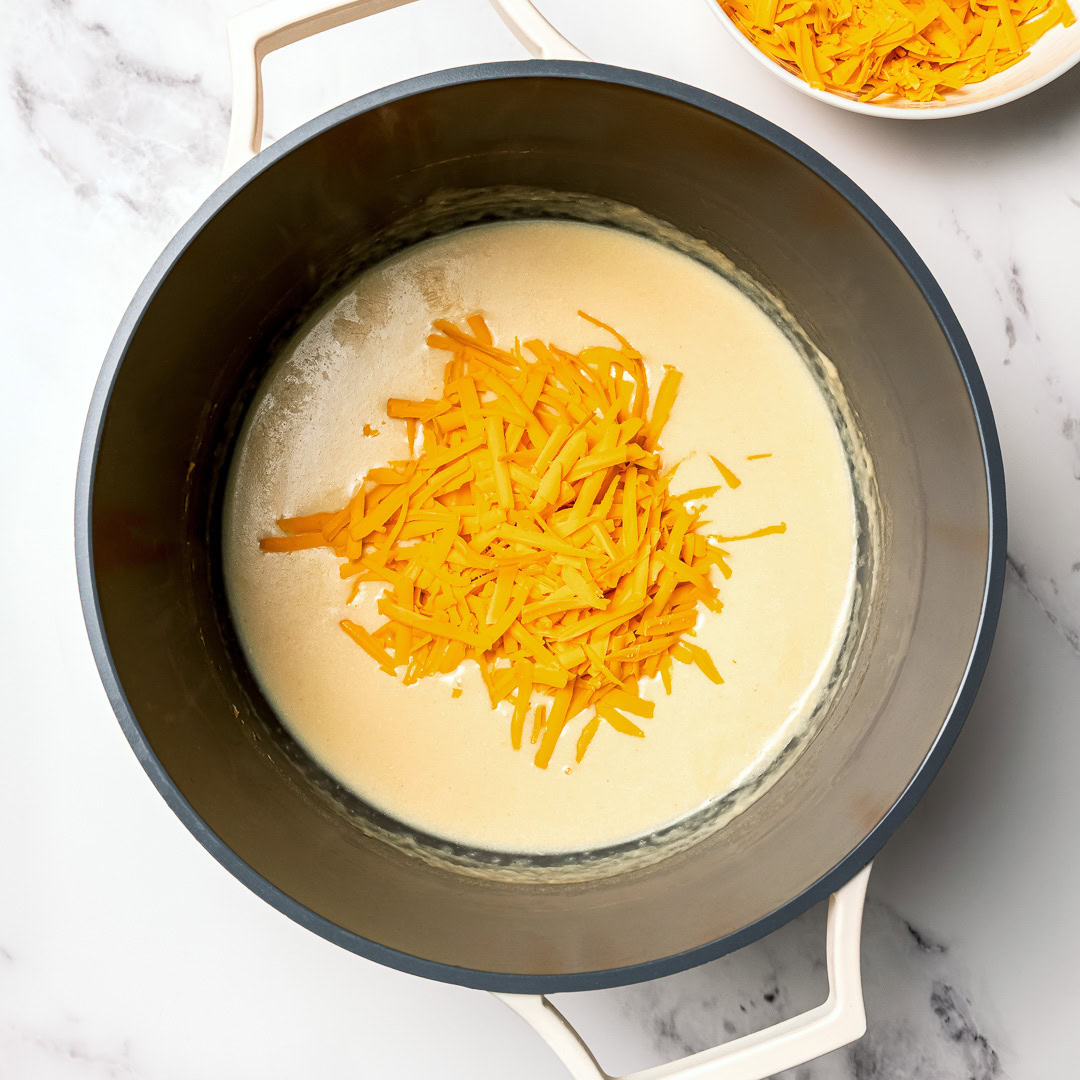 Shredded vegan cheddar added to pot of sauce.