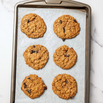 Vegan oatmeal raisin cookies on parchment lined baking sheet.