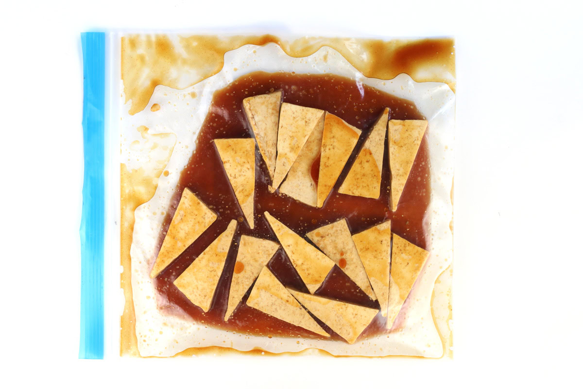 Tofu triangles marinating in a bag with sesame marinade.
