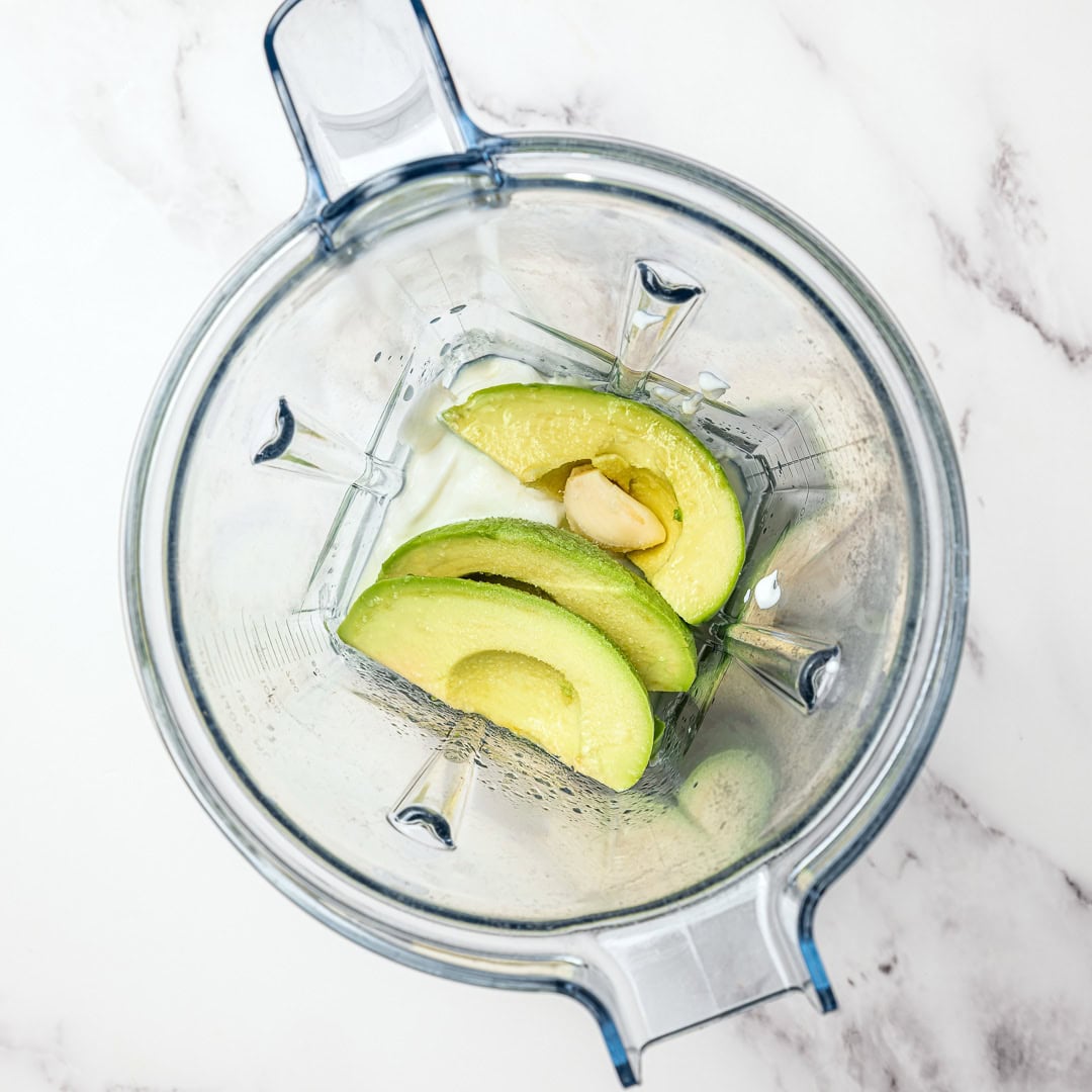 Creamy dairy-free avocado crema made in 5 minutes! Perfect for tacos, bowls, nachos, and more. Fresh, tangy, and super easy to make. Blender jar with ingredients for avocado crema.