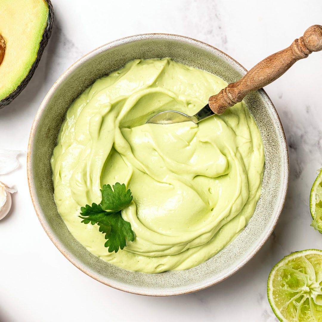 Creamy dairy-free avocado crema made in 5 minutes! Perfect for tacos, bowls, nachos, and more. Fresh, tangy, and super easy to make. Spoon in bowl of avocado crema.