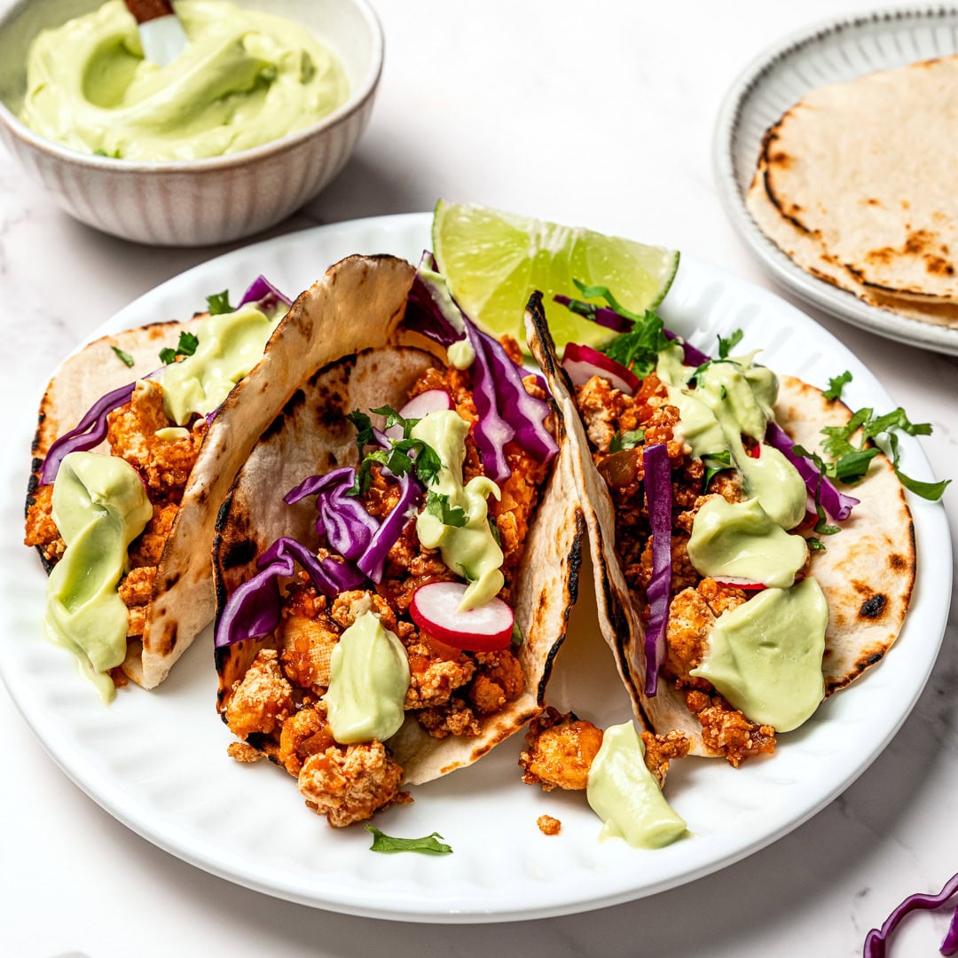 Colorful tofu tacos with avocado crema drizzle.