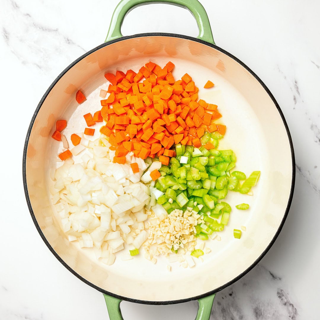 This easy lentil soup is a cozy one-pot recipe made with simple pantry ingredients! A hearty, healthy vegan meal perfect for meal prep. Garlic, carrot, celery, and onion in Dutch oven.