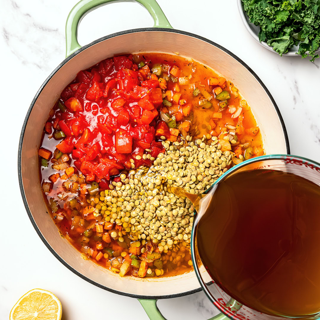 This easy lentil soup is a cozy one-pot recipe made with simple pantry ingredients! A hearty, healthy vegan meal perfect for meal prep. Pouring broth into pot for easy lentil soup.