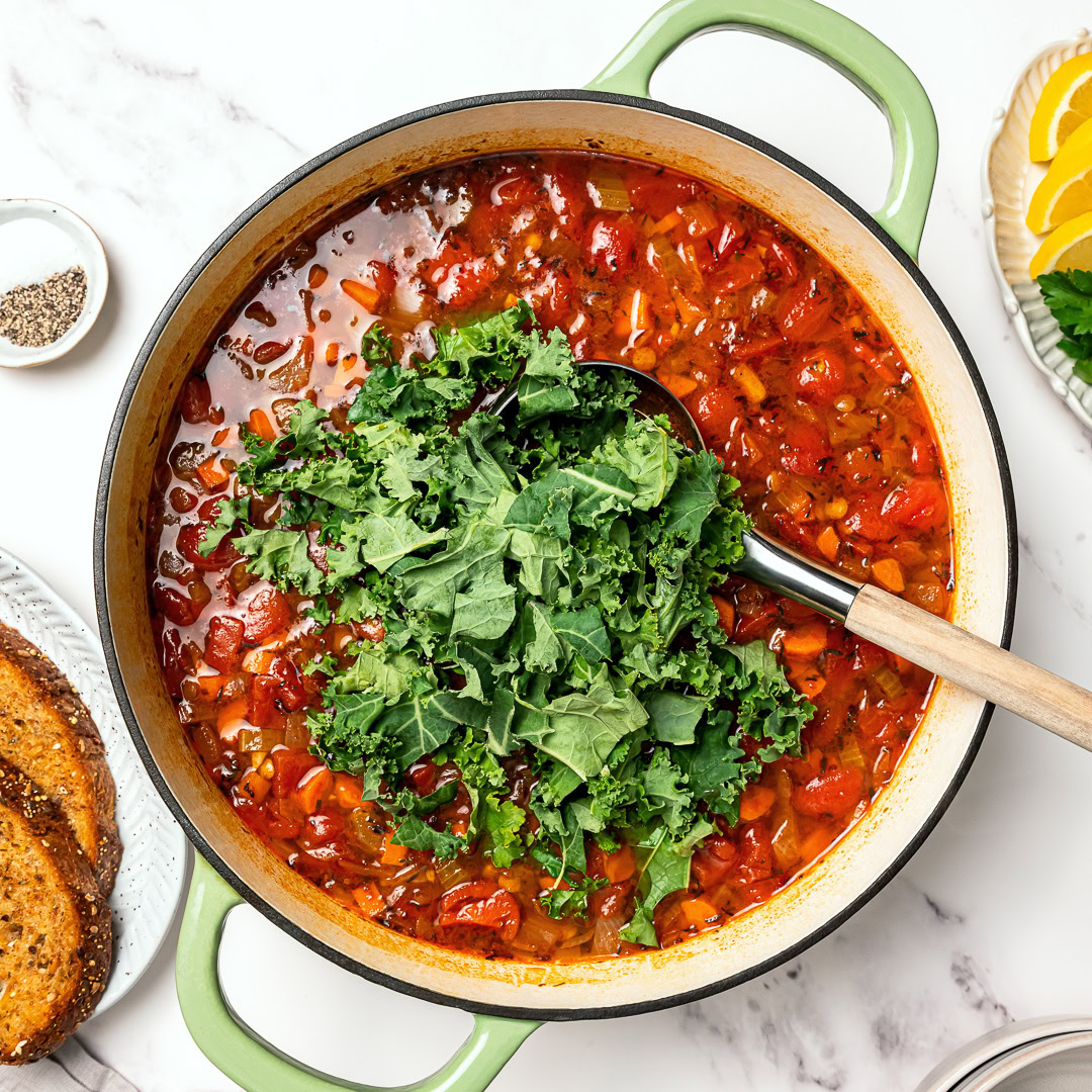 This easy lentil soup is a cozy one-pot recipe made with simple pantry ingredients! A hearty, healthy vegan meal perfect for meal prep. Kale added to lentil soup in Dutch oven.