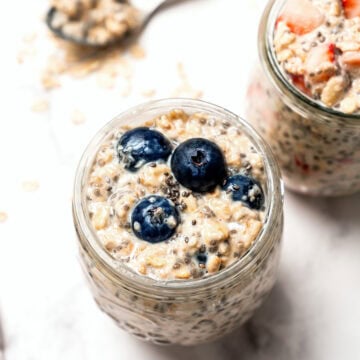 Overhead shot of two jars of overnight oats, one topped with blueberries and one topped with strawberries.