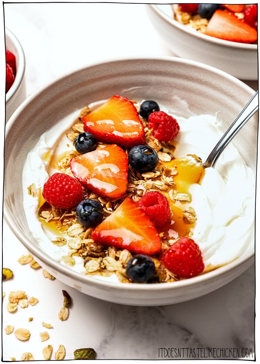 This pistachio cardamom granola is lightly sweet, perfectly crunchy, and infused with warm, aromatic cardamom. Easy 30 minute recipe! Bowl of vegan yogurt topped with pistachio cardamom granola, fresh berries, and maple syrup.
