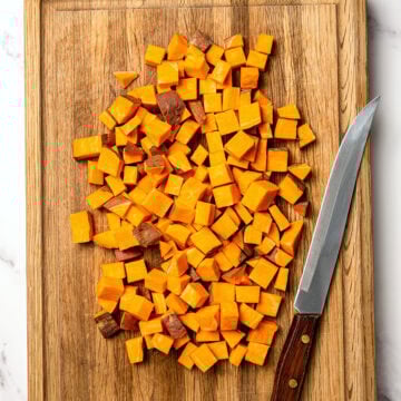 Cubed sweet potatoes on cutting board with knife.