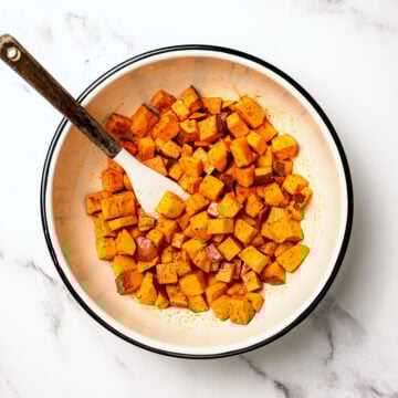 Bowl of sweet potatoes tossed with oil and seasonings.