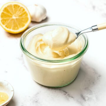 Spoonful of vegan garlic aioli held over jar with lemon and garlic.
