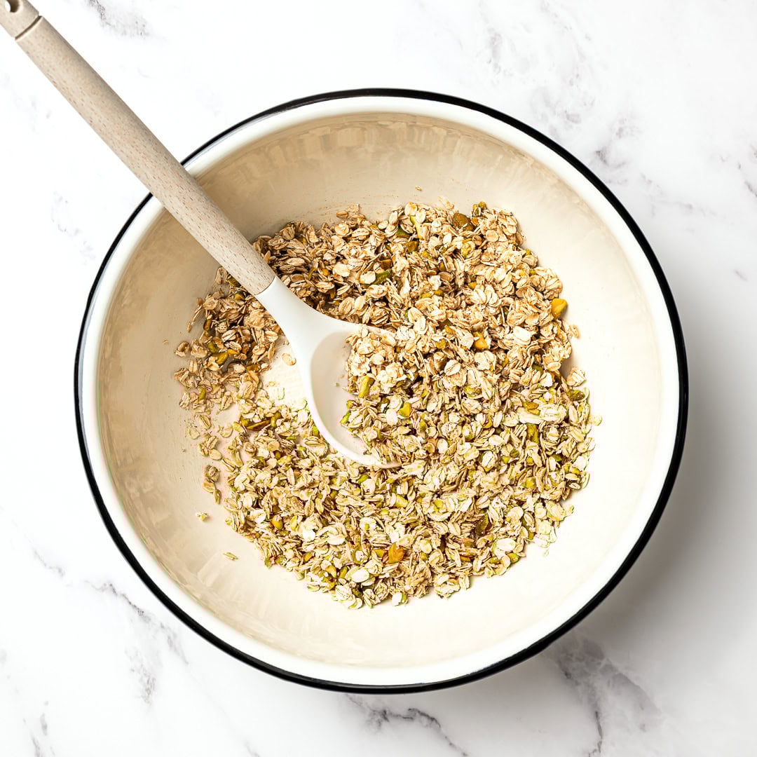 This pistachio cardamom granola is lightly sweet, perfectly crunchy, and infused with warm, aromatic cardamom. Easy 30 minute recipe! Stirring pistachio cardamom granola in mixing bowl.