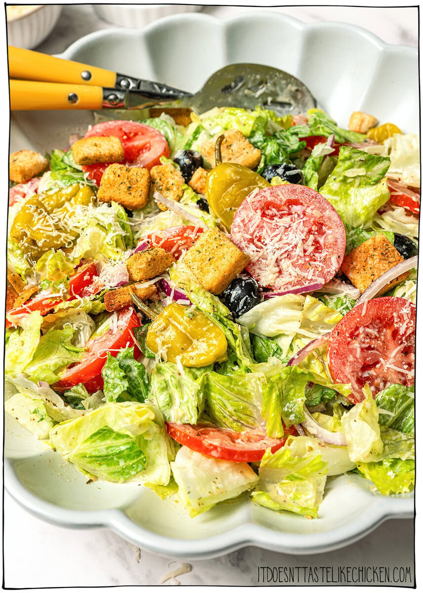 This vegan Olive Garden salad tastes just like the classic, with crisp lettuce, juicy tomatoes, olives and creamy, tangy Italian dressing! Bowl of Olive Garden salad with two spoons.