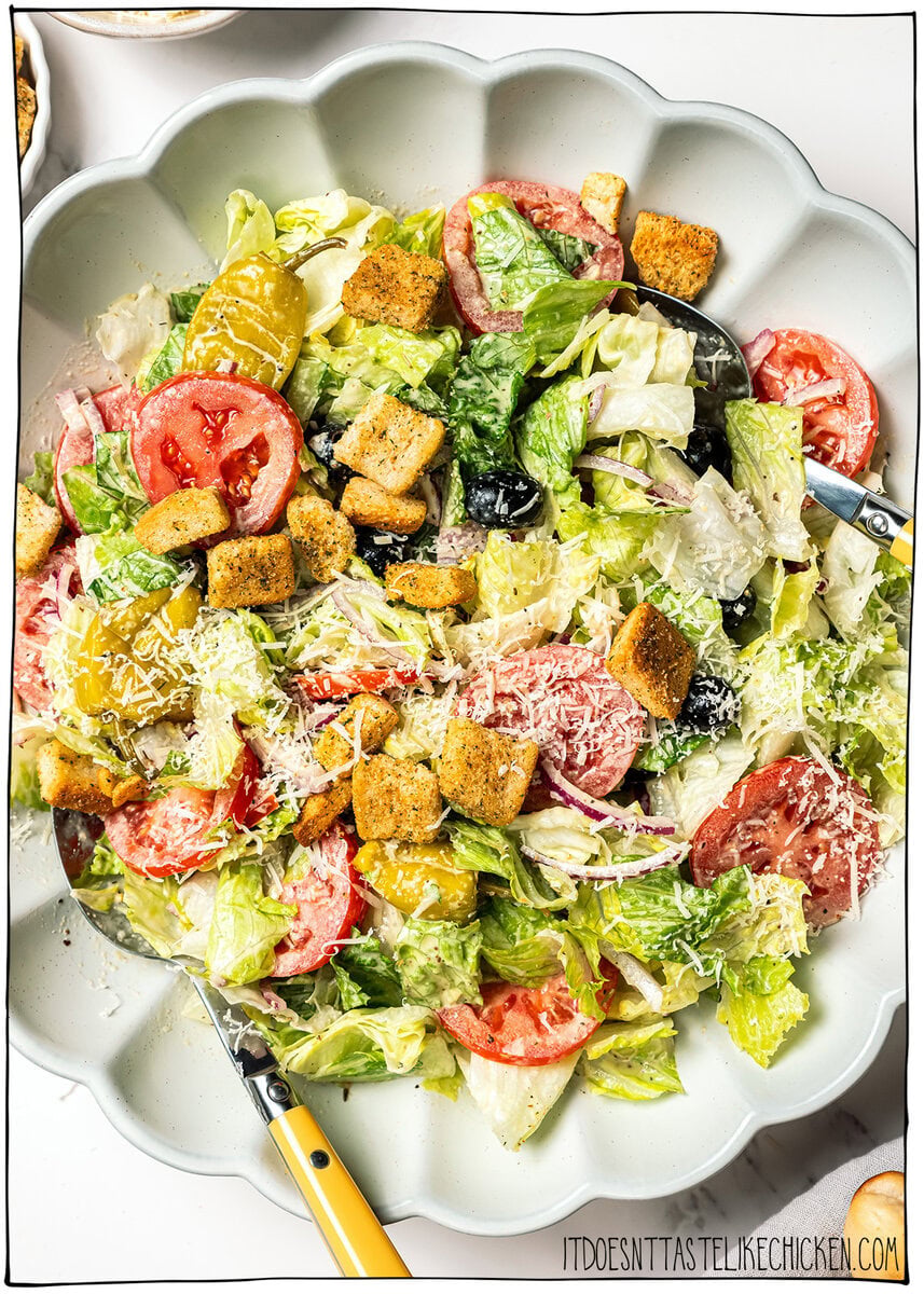 This vegan Olive Garden salad tastes just like the classic, with crisp lettuce, juicy tomatoes, olives and creamy, tangy Italian dressing! Vegan Olive Garden salad in serving bowl with spoons.