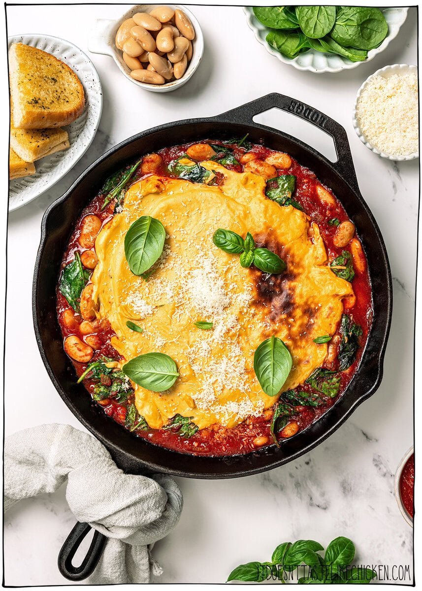 These pizza beans are an easy cozy dinner ready in 25 minutes! Creamy butter beans are simmered in marinara and topped with vegan cheese. Skillet of vegan pizza beans with fresh basil.
