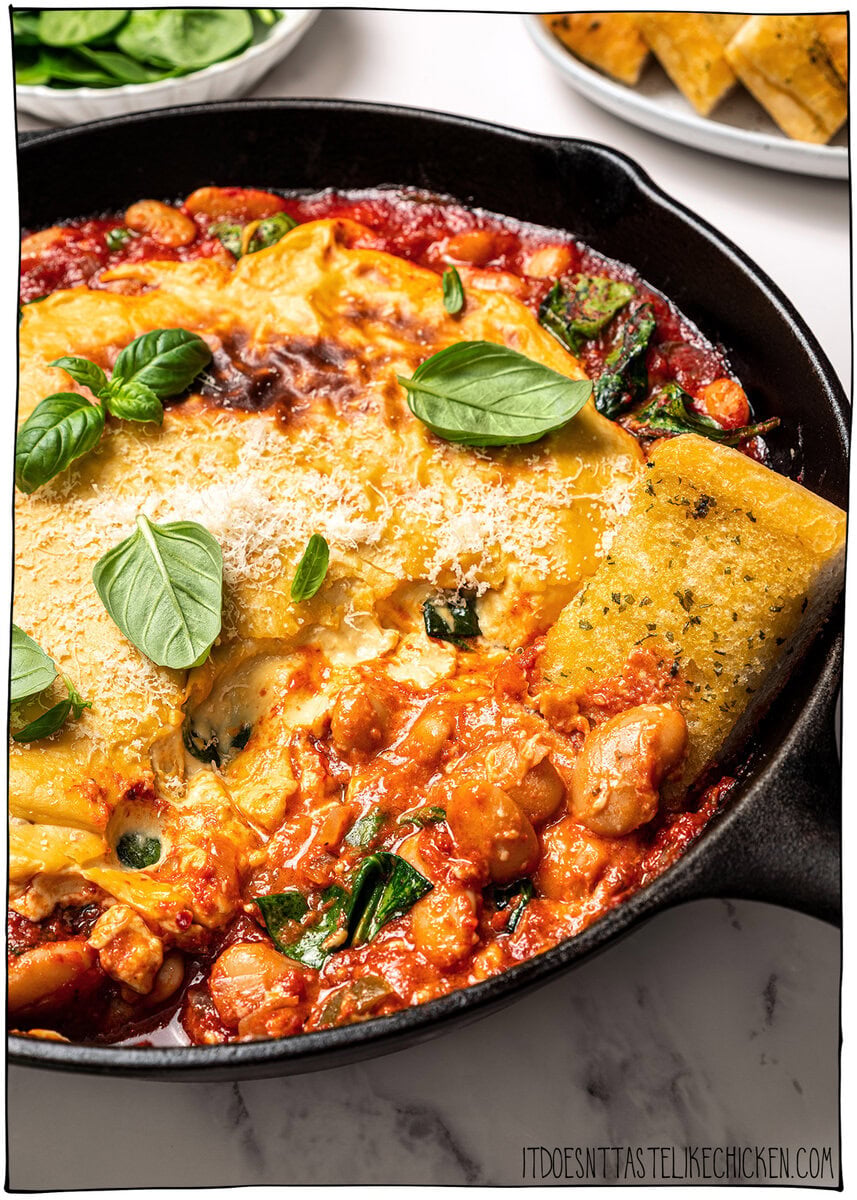 These pizza beans are an easy cozy dinner ready in 25 minutes! Creamy butter beans are simmered in marinara and topped with vegan cheese. Piece of garlic bread dipping into skillet of pizza beans.