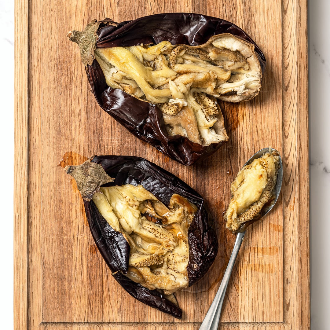 This easy baba ganoush is unbelievably creamy, smoky, and full of rich flavor, and you only need a handful of simple ingredients to make it! Scooping insides from roasted eggplant.