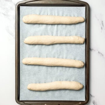 4 unbaked Olive Garden breadsticks on pan.