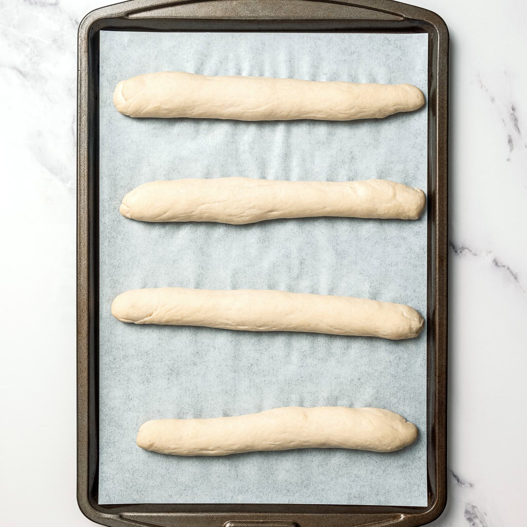 These vegan Olive Garden breadsticks are soft, fluffy, and brushed with buttery garlic salt, just like the restaurant. So irresistible! 4 unbaked Olive Garden breadsticks on pan.