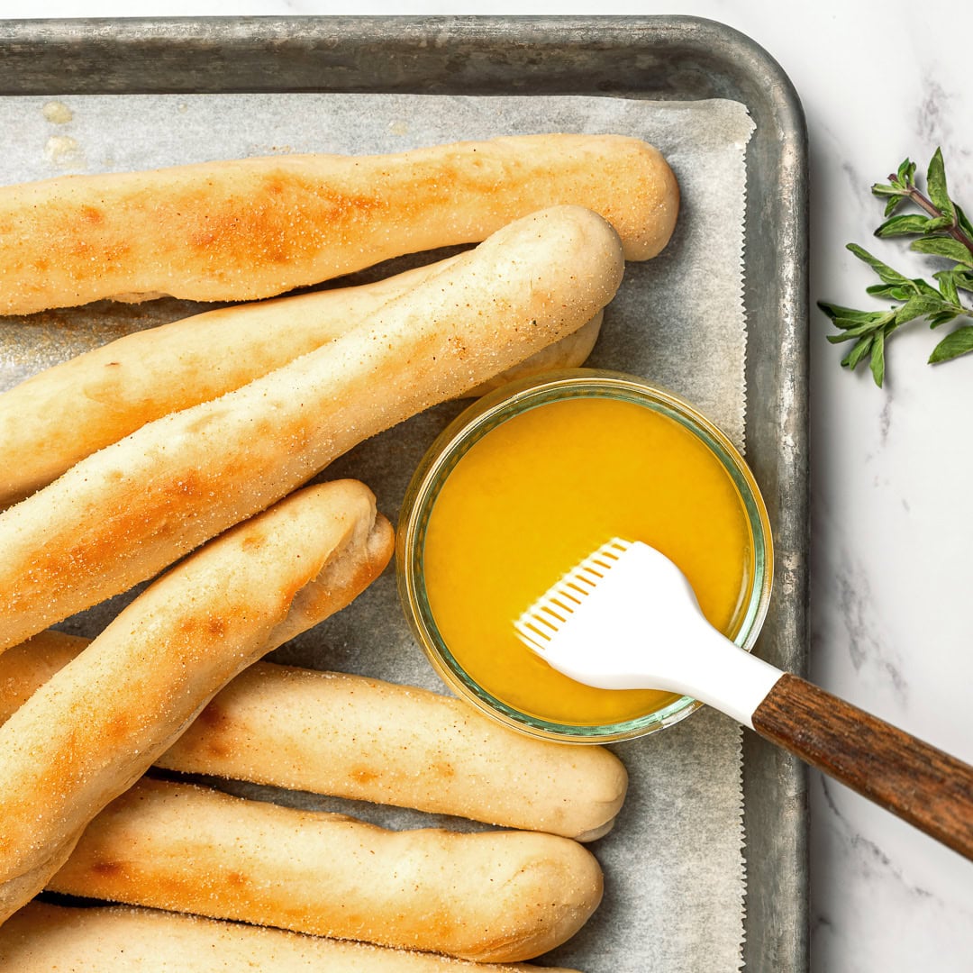 These vegan Olive Garden breadsticks are soft, fluffy, and brushed with buttery garlic salt, just like the restaurant. So irresistible! Olive Garden breadsticks on pan with melted garlic butter in bowl.