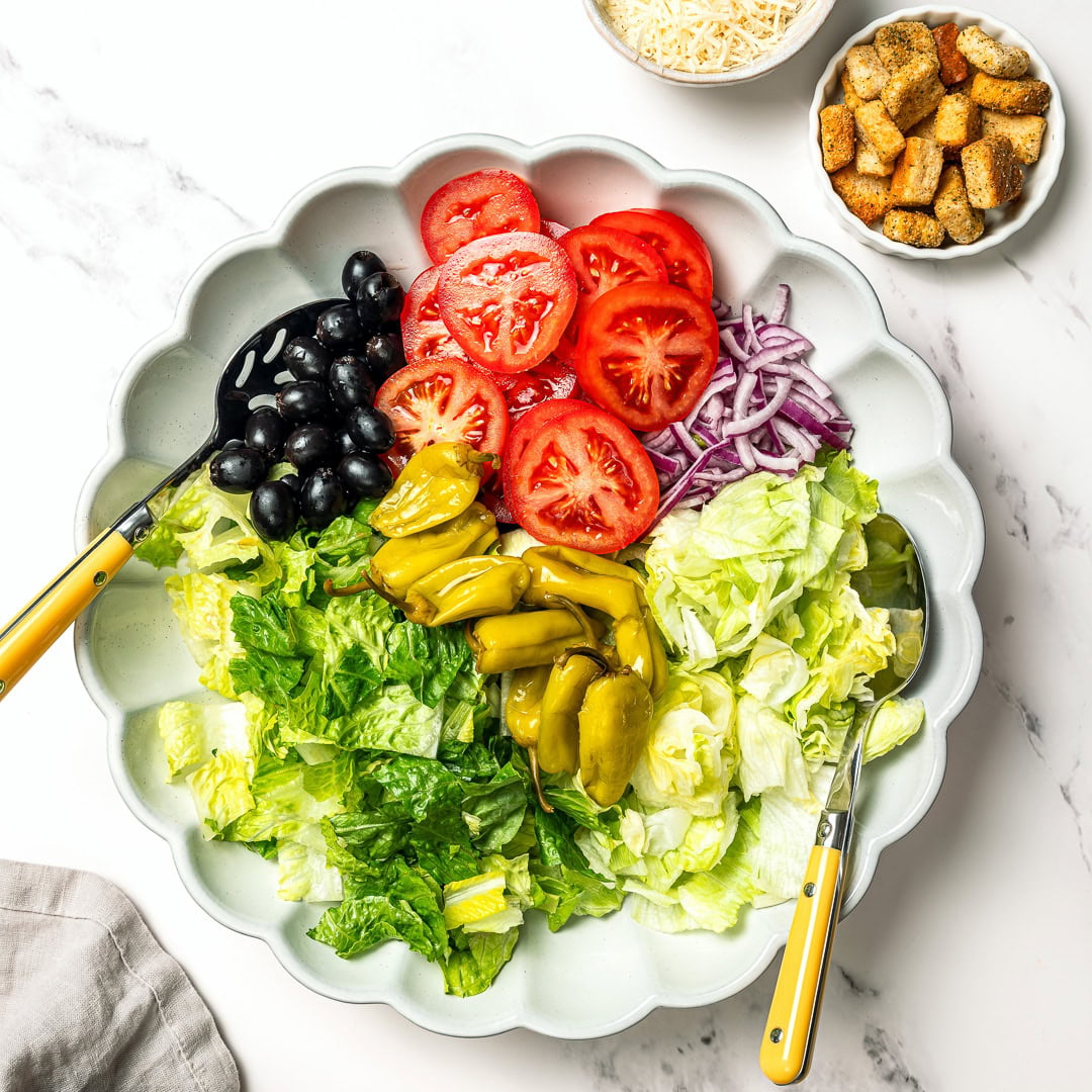 This vegan Olive Garden salad tastes just like the classic, with crisp lettuce, juicy tomatoes, olives and creamy, tangy Italian dressing! Ingredients for Olive Garden salad in bowl before tossing.