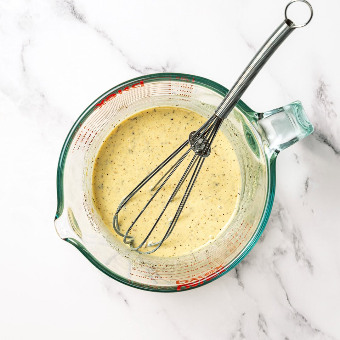This vegan Olive Garden salad tastes just like the classic, with crisp lettuce, juicy tomatoes, olives and creamy, tangy Italian dressing! Creamy Italian dressing in liquid measuring cup with whisk.