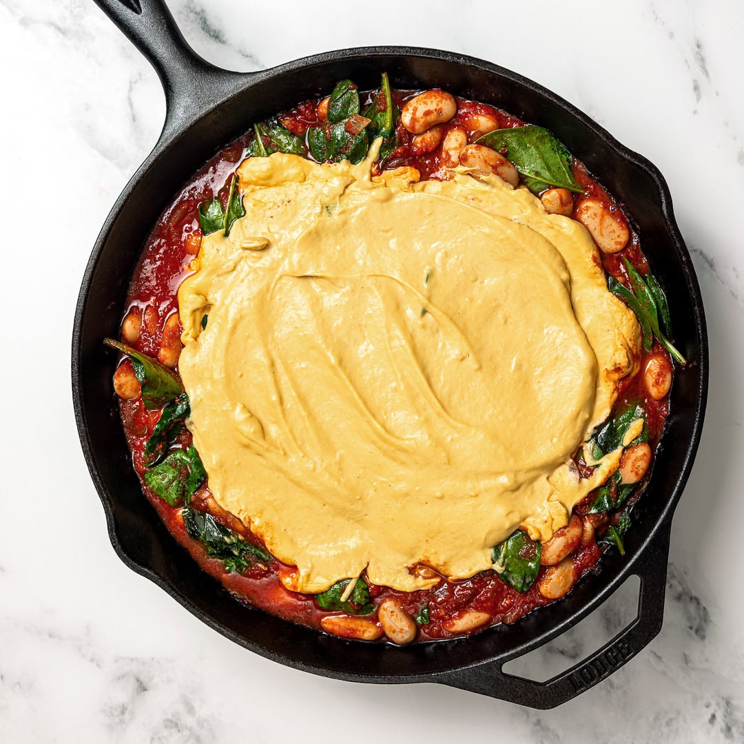 These pizza beans are an easy cozy dinner ready in 25 minutes! Creamy butter beans are simmered in marinara and topped with vegan cheese. Vegan cheese sauce added to skillet of pizza beans.
