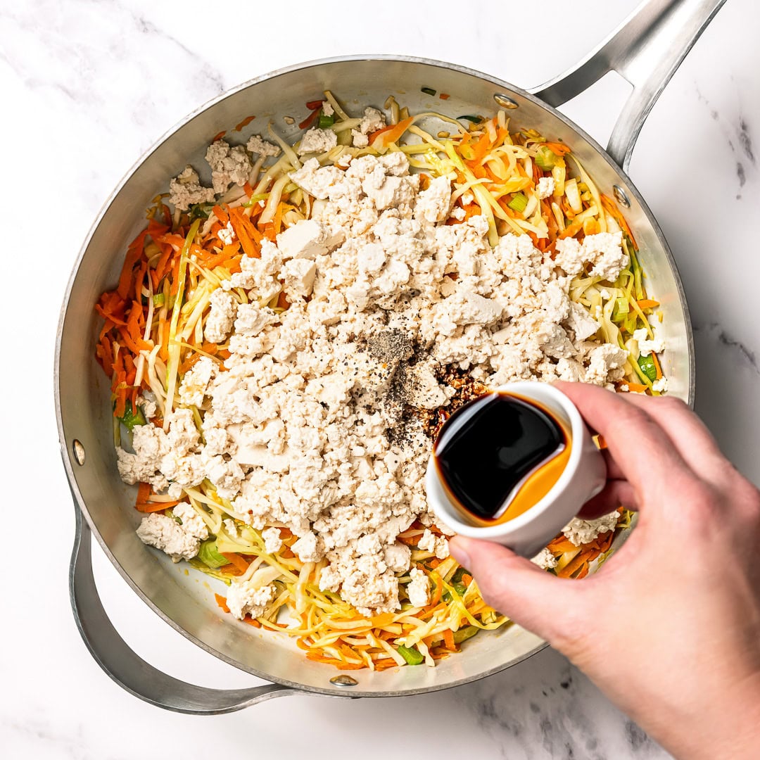 These vegan rice paper dumplings are crispy on the outside, chewy around the edges, with a savory cabbage and tofu filling. Viral on TikTok! Pouring soy sauce into skillet of tofu, cabbage, and carrots.