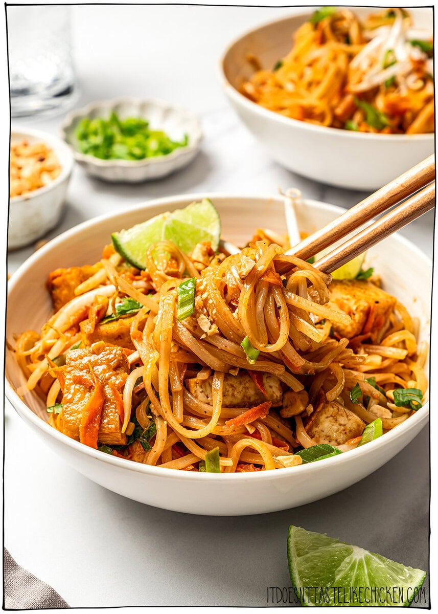 Chopsticks lifting tofu pad thai from bowl.