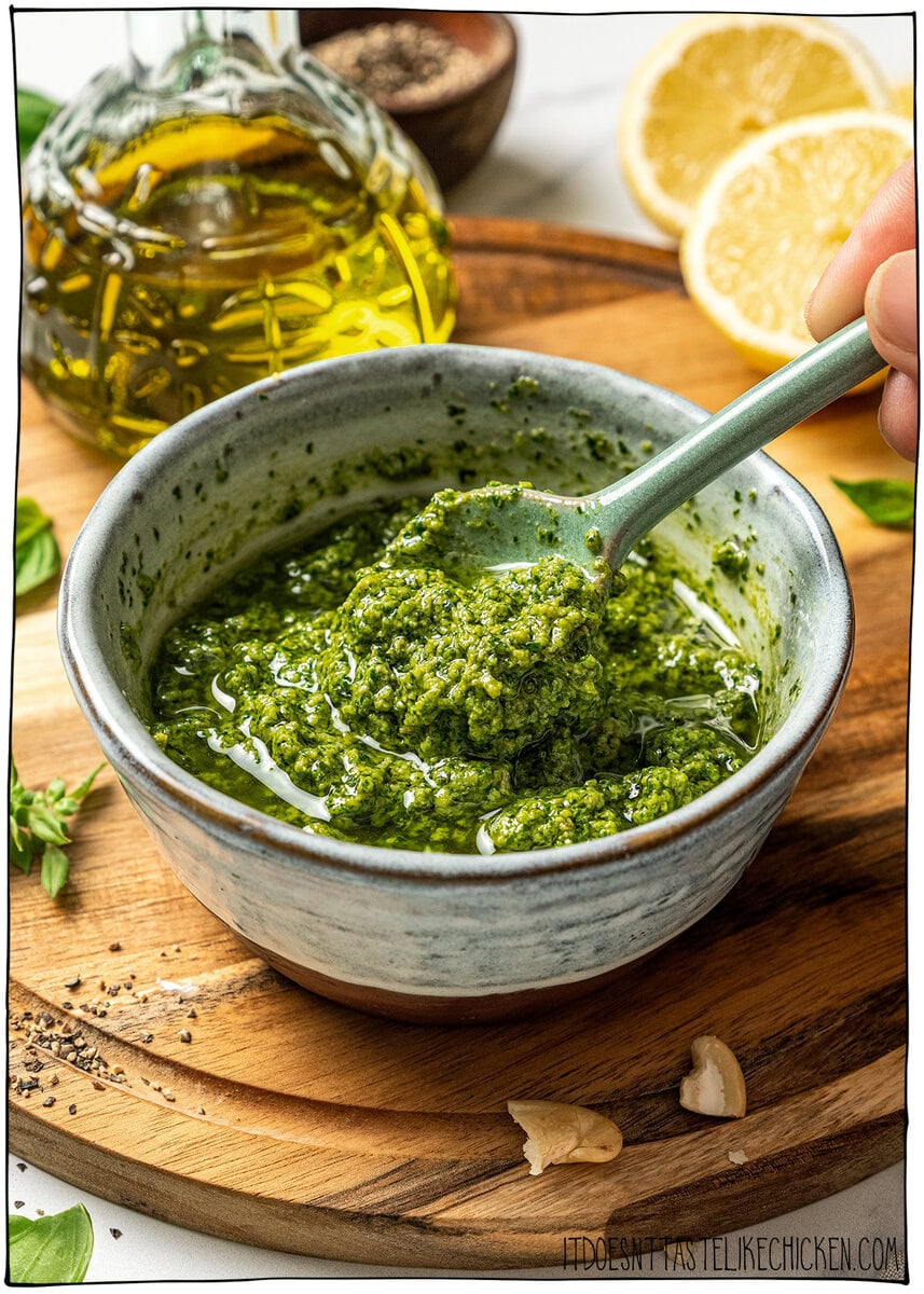 This creamy vegan pesto is rich, vibrant, and packed with fresh basil flavor, just like classic pesto, but completely dairy-free! Bowl of vegan pesto with spoon on cutting board.