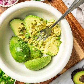 Fork mashing avocados in bowl.