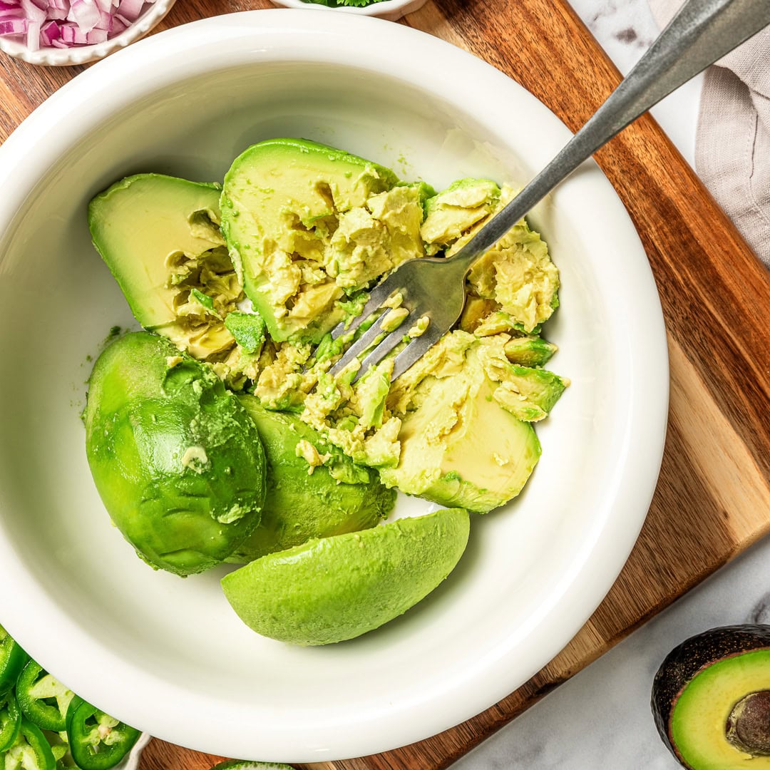 This easy Chipotle guacamole recipe is creamy, bright, and packed with fresh flavor, just like the restaurant version. Only 5 ingredients! Fork mashing avocados in bowl.