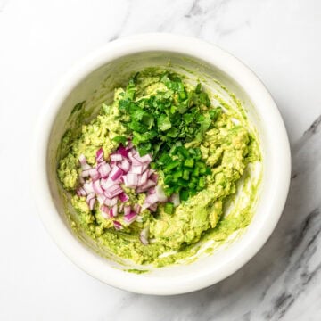 Red onion and cilantro added to bowl of guacamole.