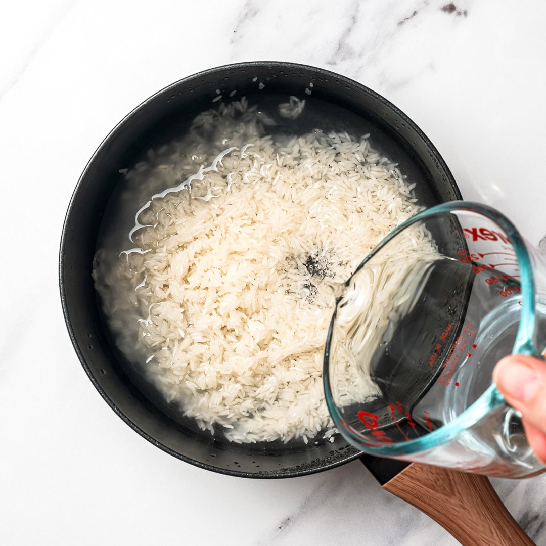 This easy Chipotle rice recipe is fluffy, lightly seasoned, and finished with fresh lime juice and cilantro for that signature fresh flavor! Pouring water into pot of rice.
