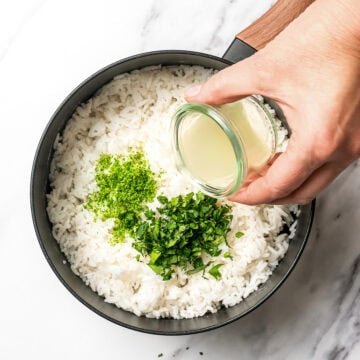 Pouring lime juice into pot of rice with lime zest and cilantro.
