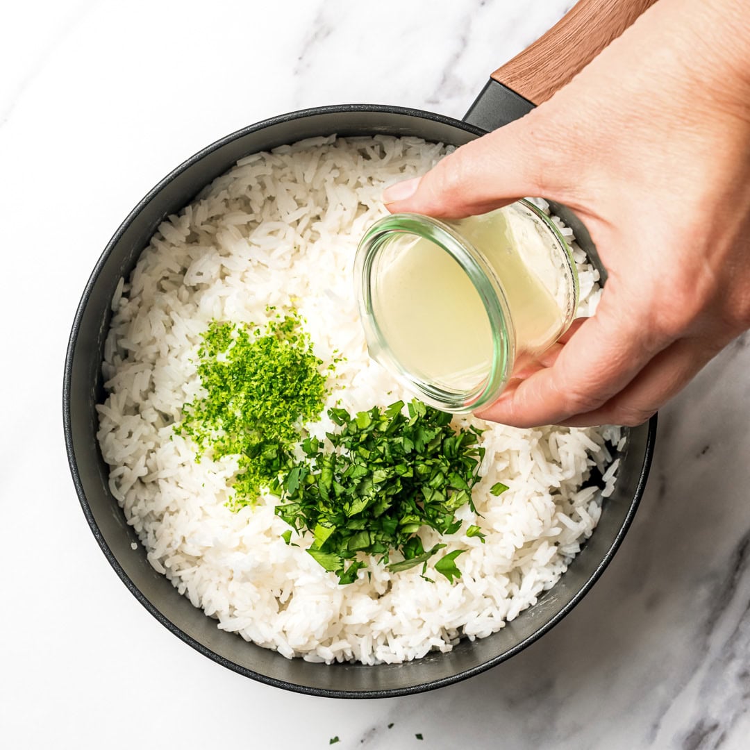 This easy Chipotle rice recipe is fluffy, lightly seasoned, and finished with fresh lime juice and cilantro for that signature fresh flavor! Pouring lime juice into pot of rice with lime zest and cilantro.