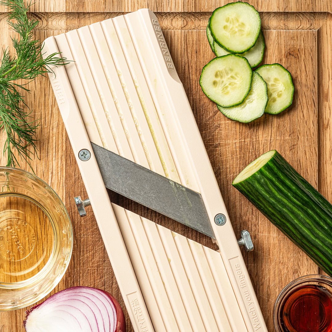 This easy cucumber dill salad is light, crisp, and refreshing, made with thinly sliced cucumbers, red onion, and a simple tangy vinaigrette. Mandoline slicer on cutting board with cucumber.