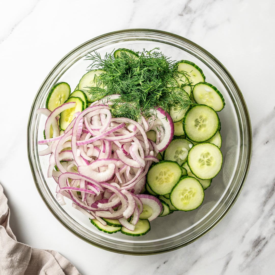 This easy cucumber dill salad is light, crisp, and refreshing, made with thinly sliced cucumbers, red onion, and a simple tangy vinaigrette. Cucumbers, dill, and red onion in glass bowl.