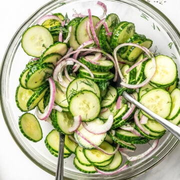 Cucumber dill salad in glass bowl with two spoons for tossing.