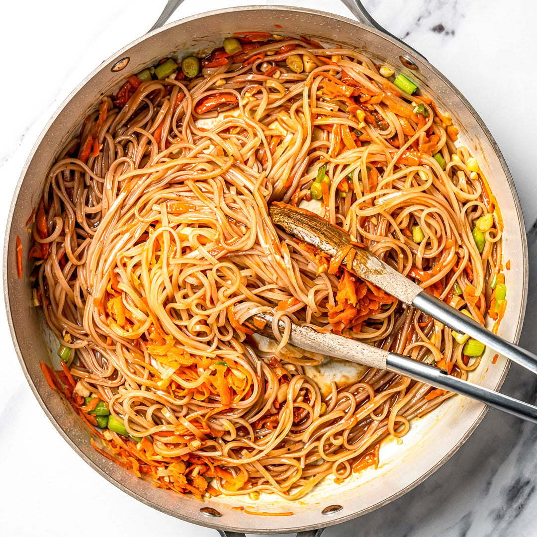 Sauce and noodles added to pan with vegetables for pad thai.