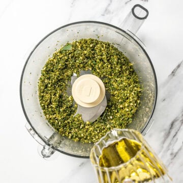 Drizzling olive oil into food processor with pesto.
